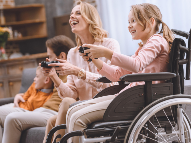 happy family with disabled child in wheelchair playing with joysticks together at home